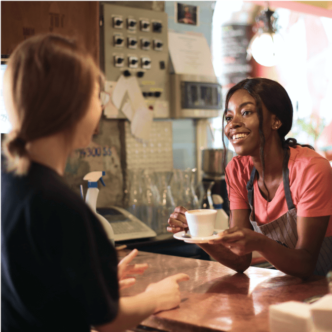 Une femme brune sert du café à un client dans un café.