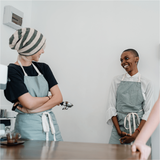 Deux femmes portant des tabliers se sourient dans un café.