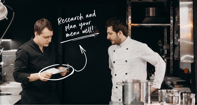 Two chefs standing in restaurant kitchen looking at a menu
