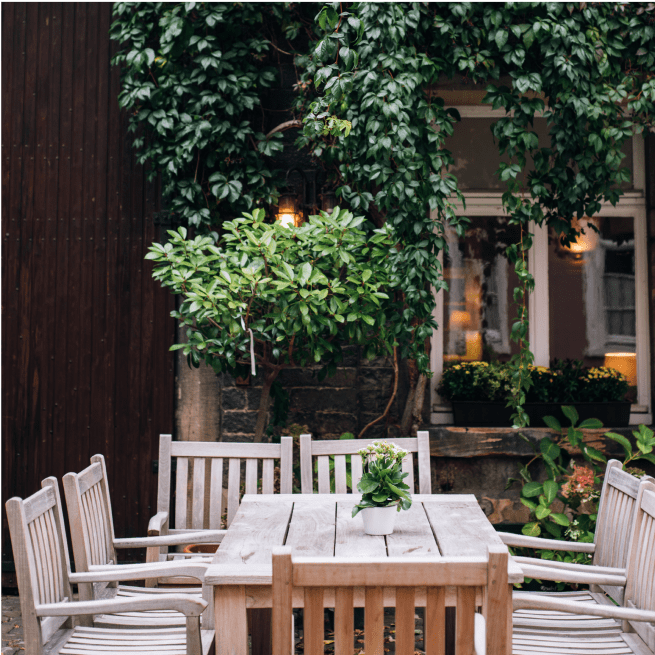 Une table en bois entourée de chaises dans une cour décorée de plantes.