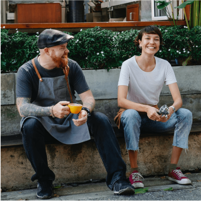 Deux baristas sourient et sont assis sur un banc.