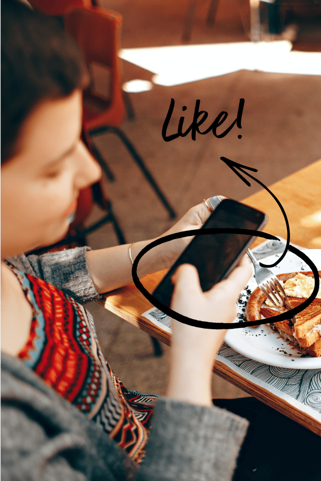 A person using their phone at a restaurant table with food, suggesting social media engagement with the prompt "Like!",