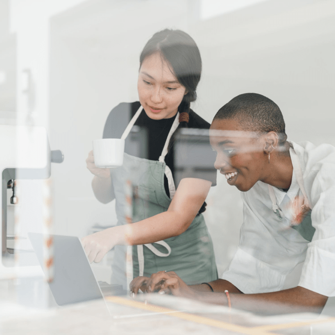 Two chefs looking at a laptop with one pointing at the screen and the other typing