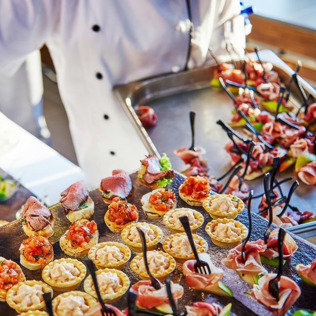 Um chefe de cozinha profissional segurando travessas com diversas tortinhas e pequenos aperitivos.