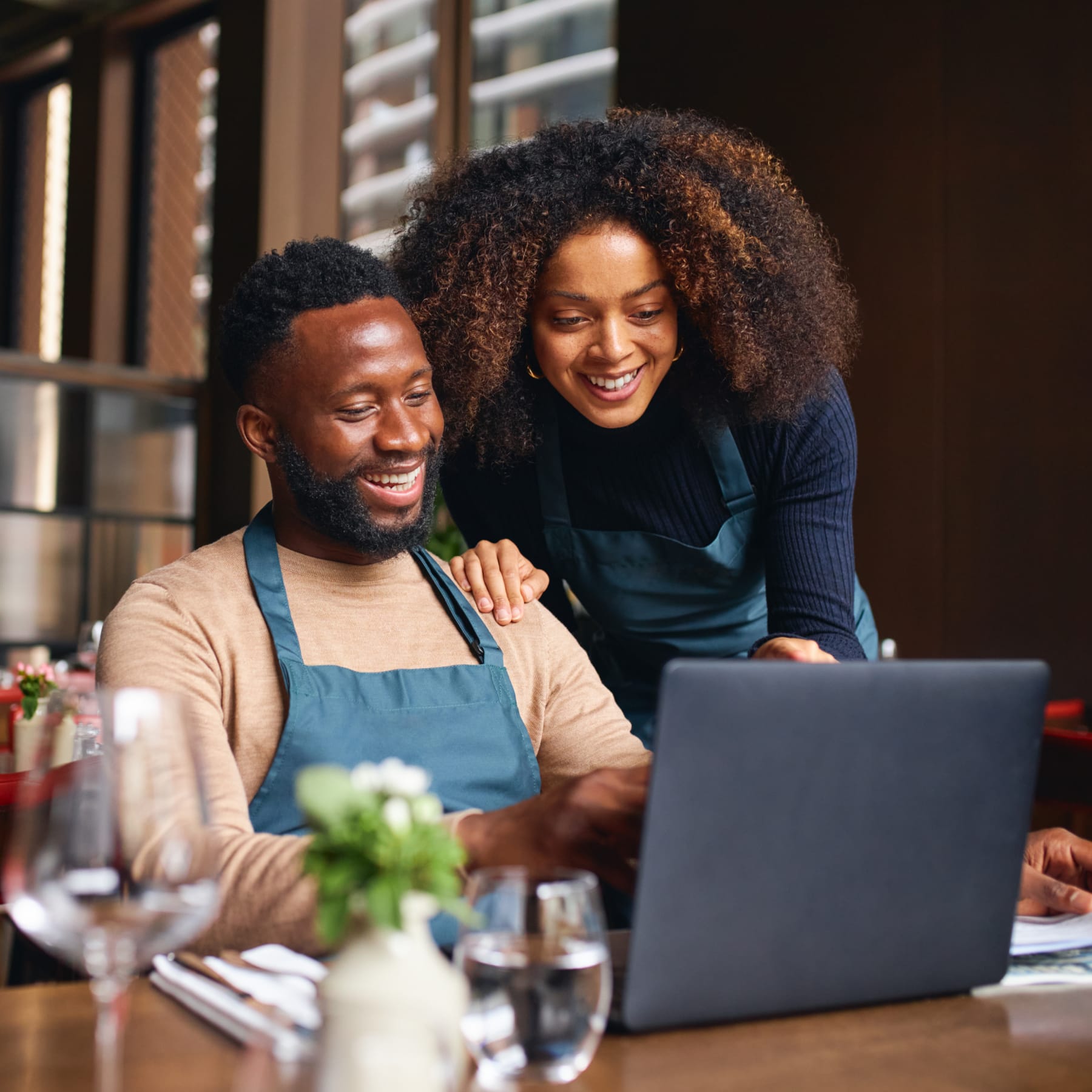 Two restaurant owners wearing aprons look at a laptop.