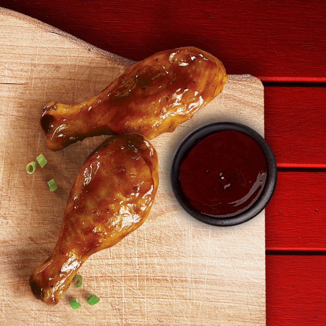 Two chicken legs with a small A1 sauce cup on a wooden board