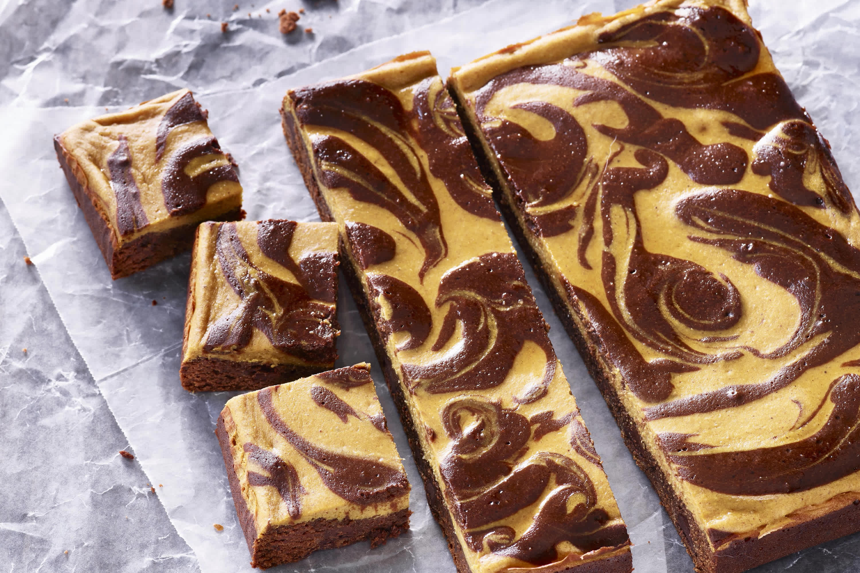 Marbled pumpkin and chocolate cheesecake bars sliced on parchment paper.