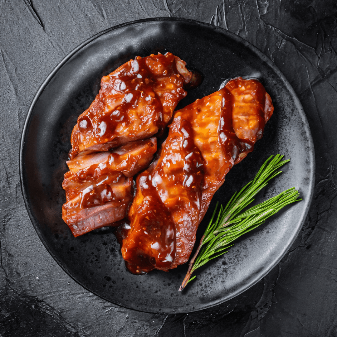 Grilled ribs with rosemary on a black plate.