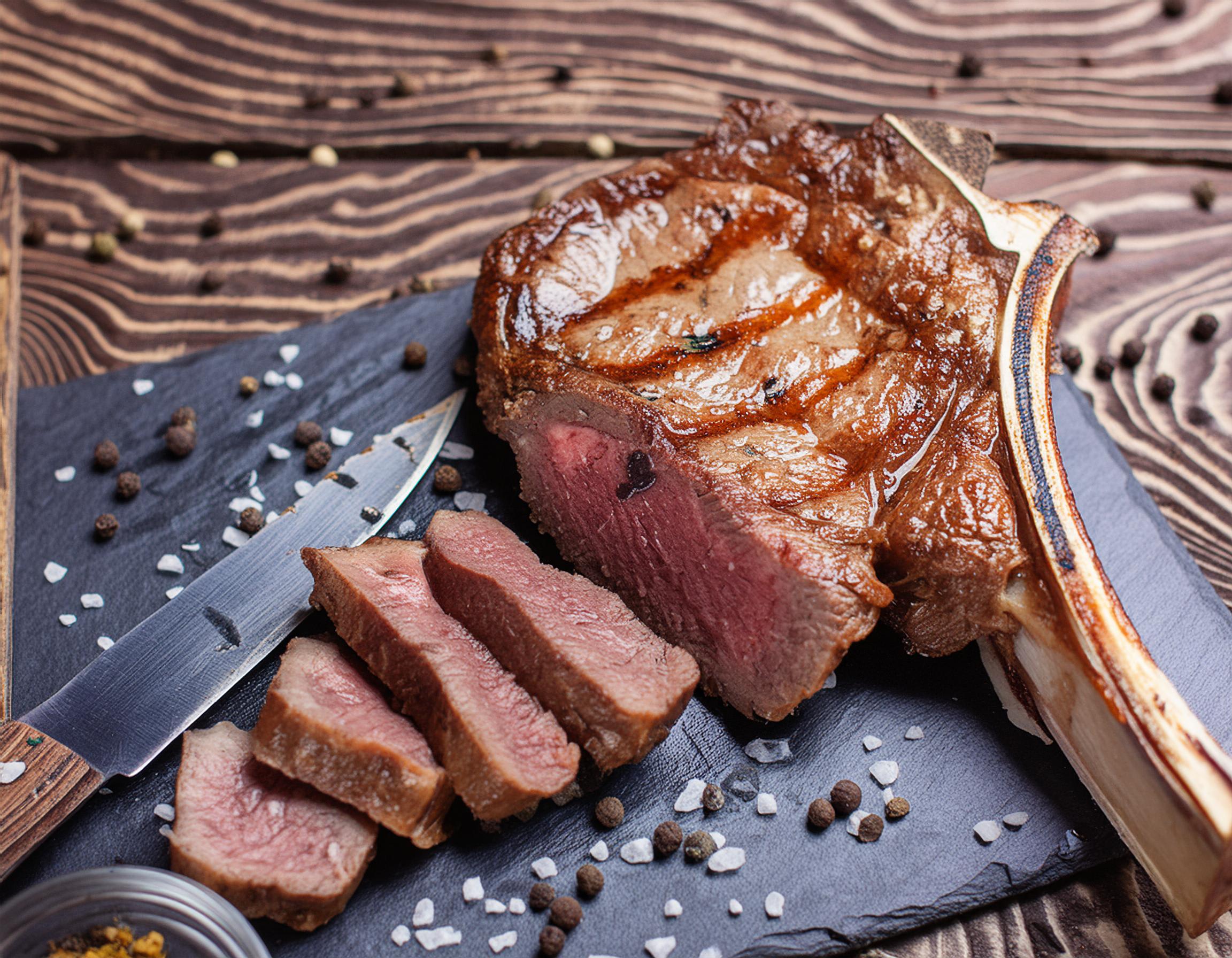 Gegrilltes T-Bone-Steak, teilweise aufgeschnitten, serviert auf einer dunklen Schieferplatte.