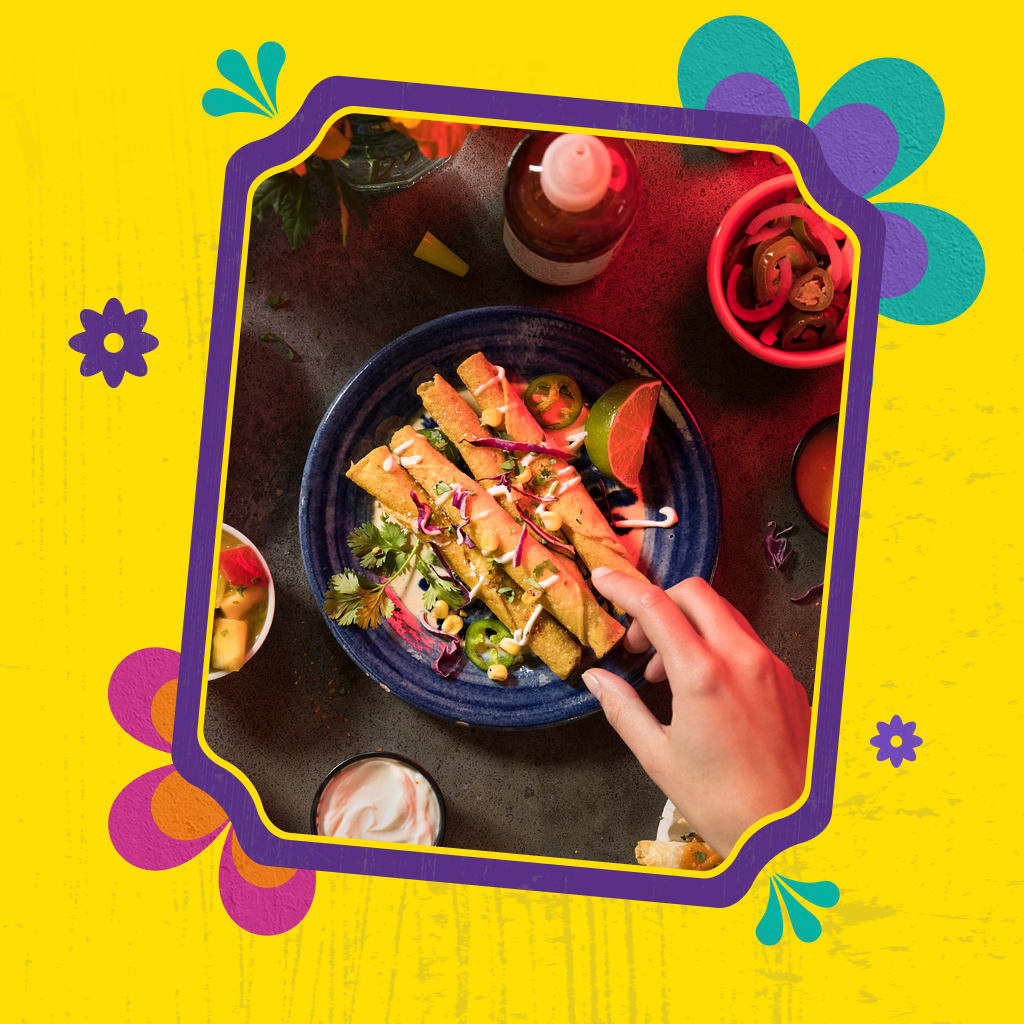 A hand reaches for a plate of crispy flautas on a colorful yellow background.