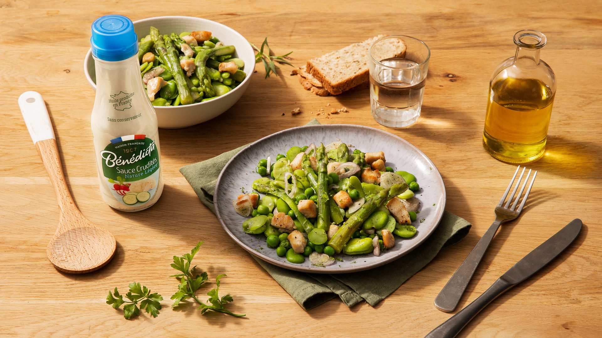 Salade verte avec fèves, asperges et poulet grillé, accompagnée d'un verre d'eau et de pain.
