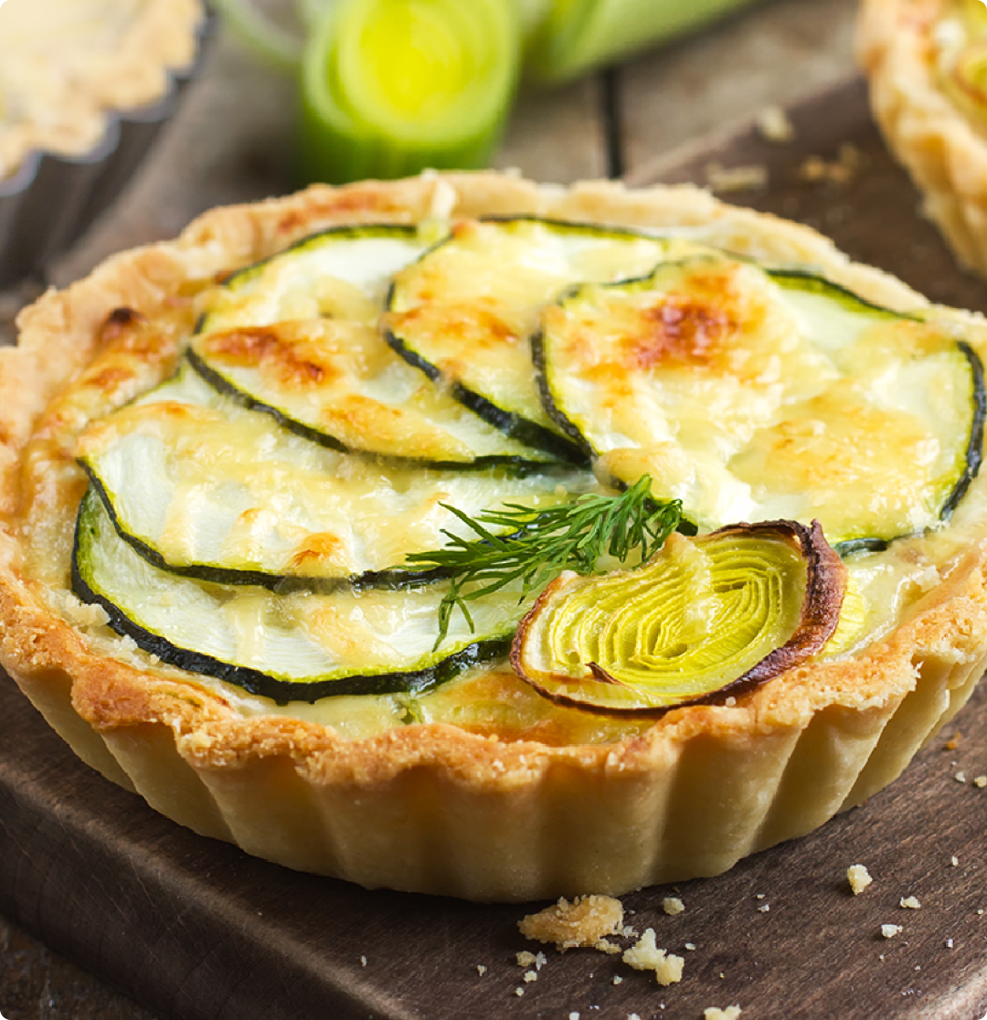 Torta con zucchine e porri su tagliere di legno.