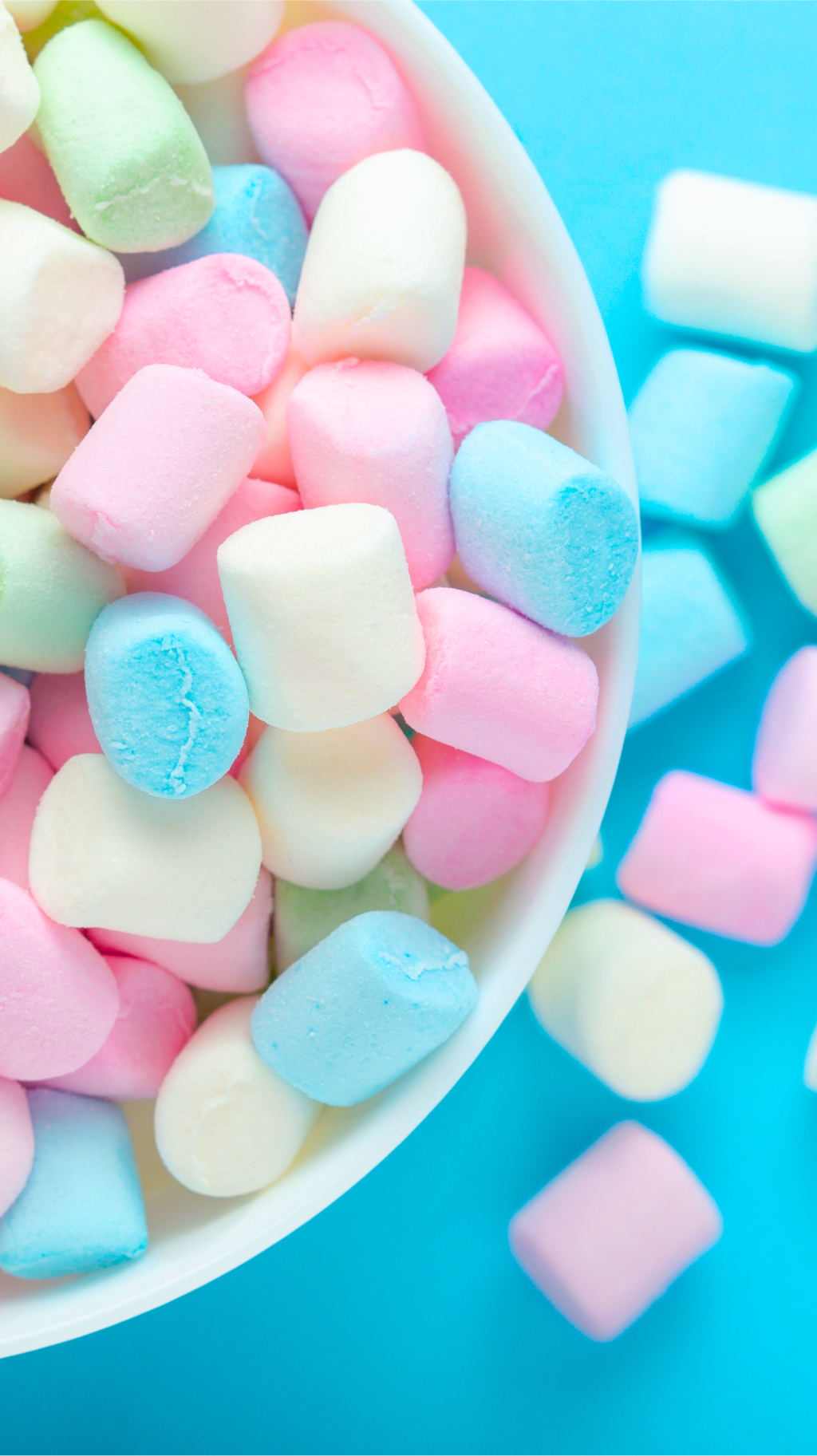 Green, blue, pink, yellow and white Jet Puffed marshmallows in a bowl on a blue background