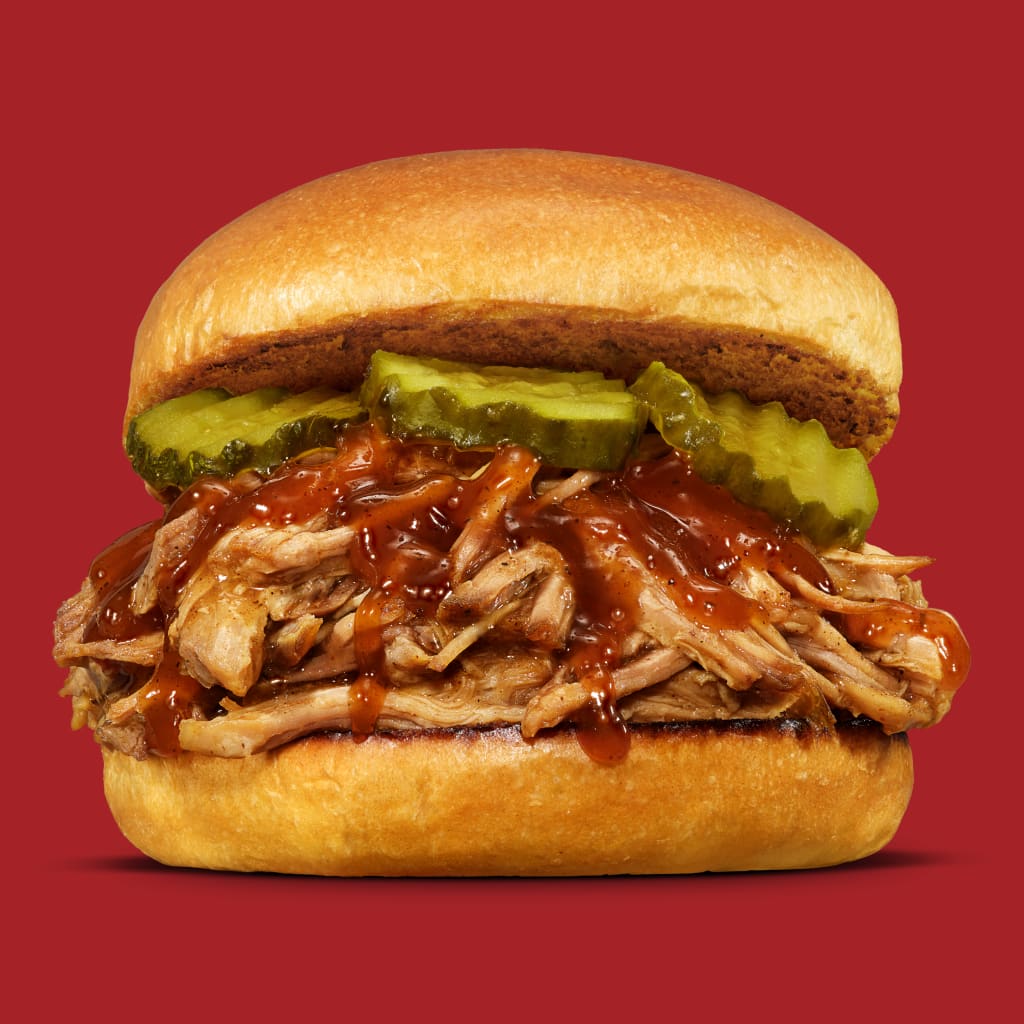 Pulled pork sandwich with pickles on a red background.
