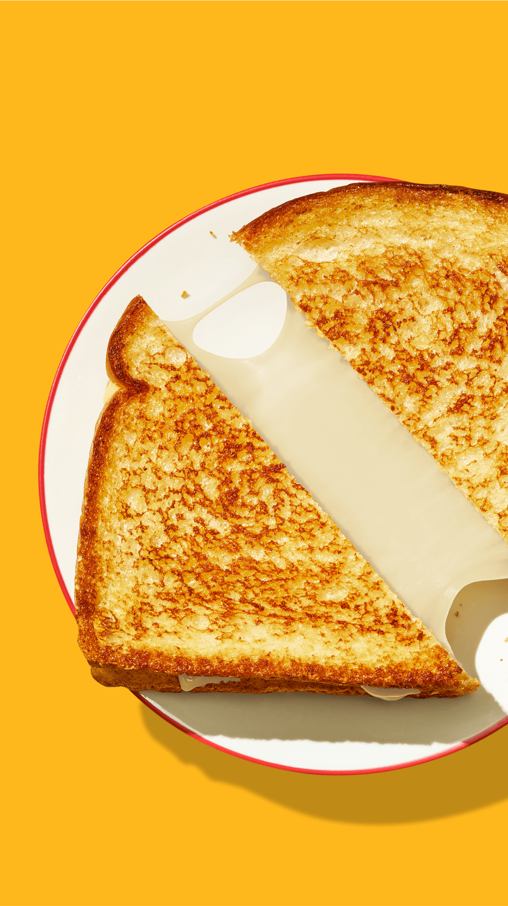 A split grilled cheese sandwich on a plate on a yellow background