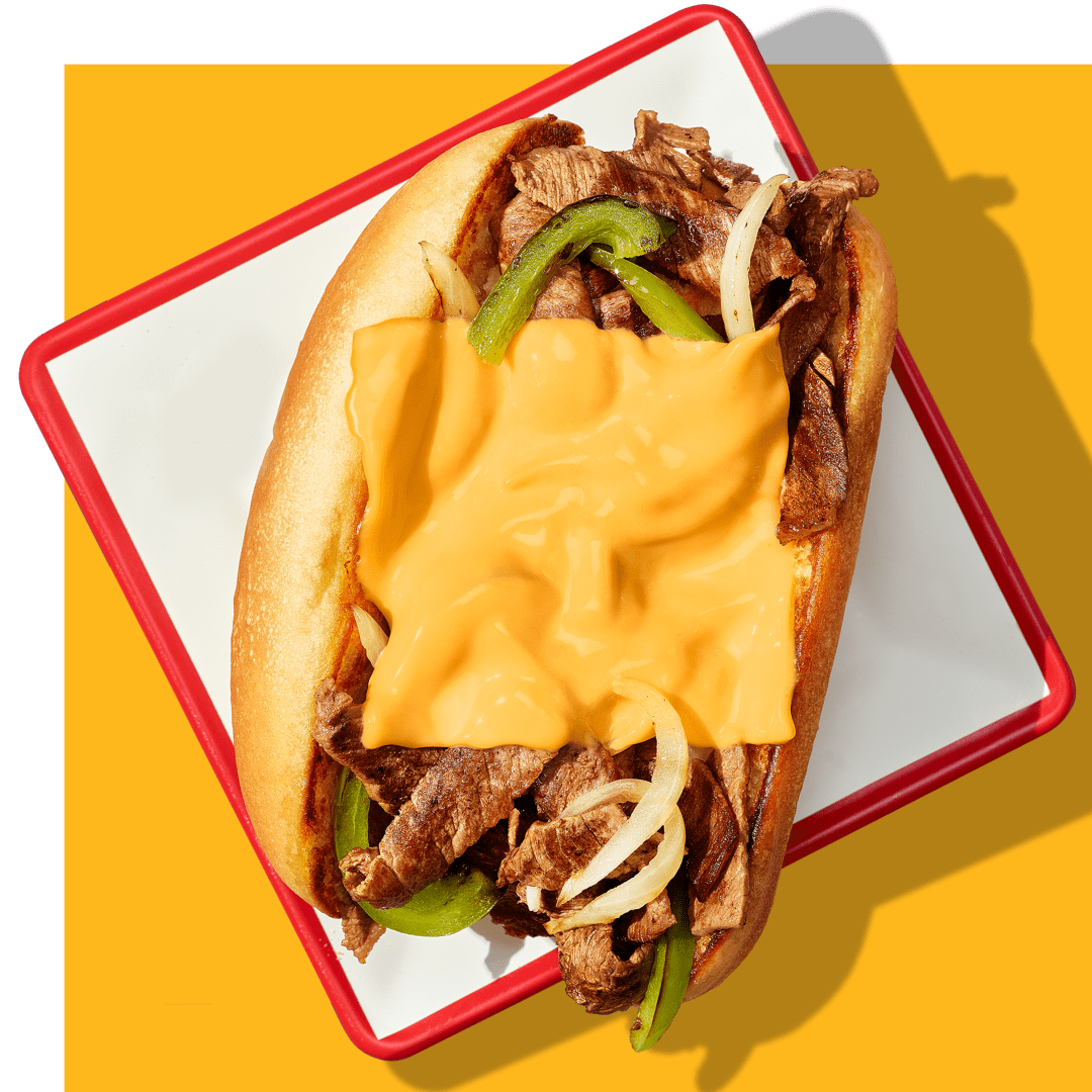 Image of a cheesesteak sandwich with melted cheese, peppers, and onions on a tray.