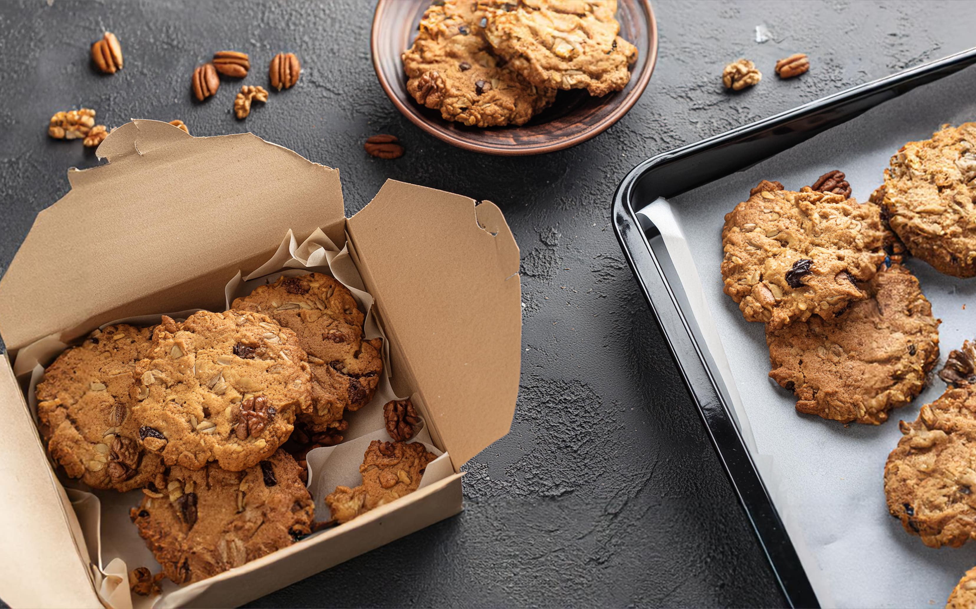 Versgebakken havermoutkoekjes met walnoten en rozijnen in een kartonnen doos op een donkere tafel.