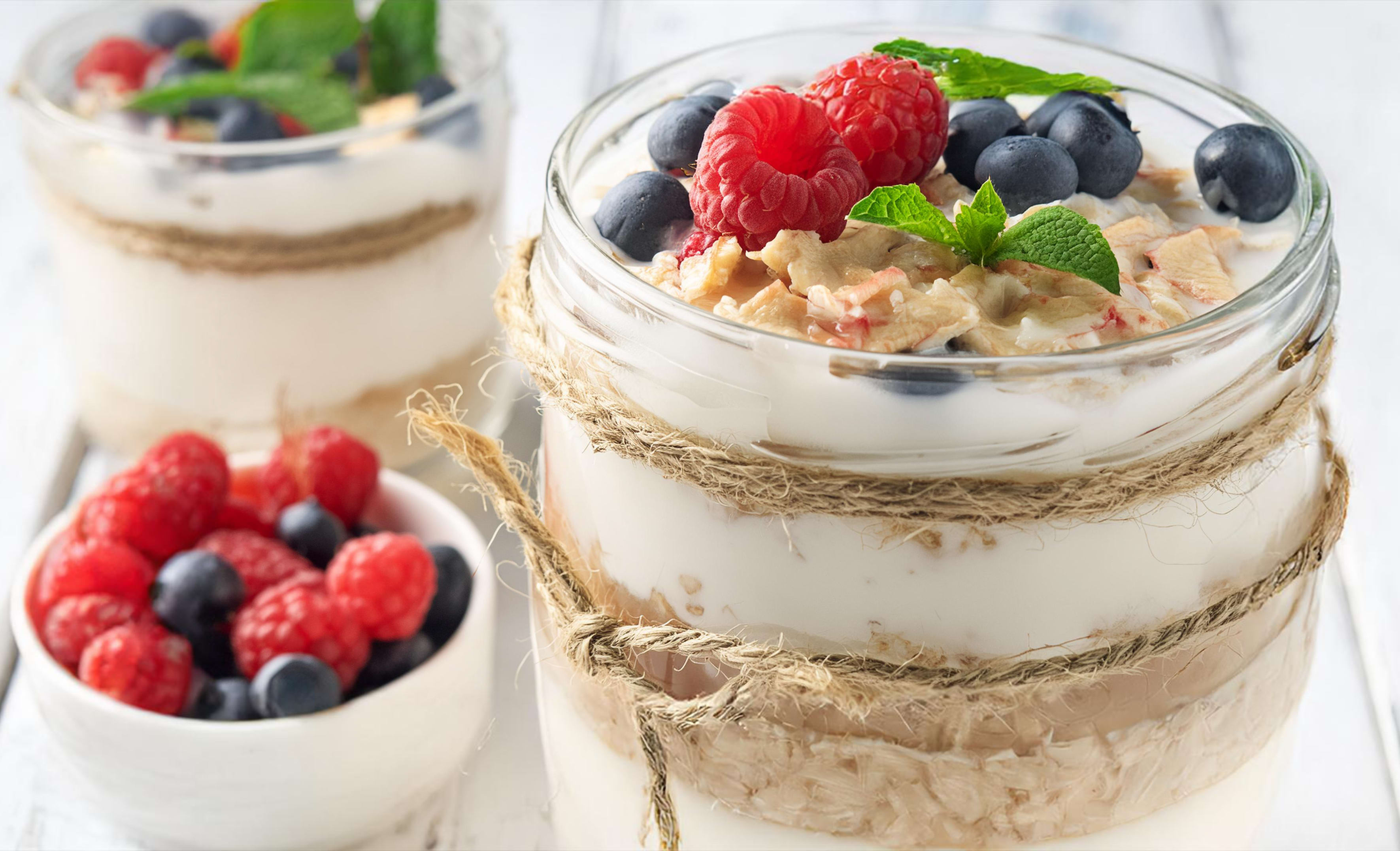 Glazen pot met laagjes havermout, yoghurt, frambozen en blauwe bessen, versierd met munt.