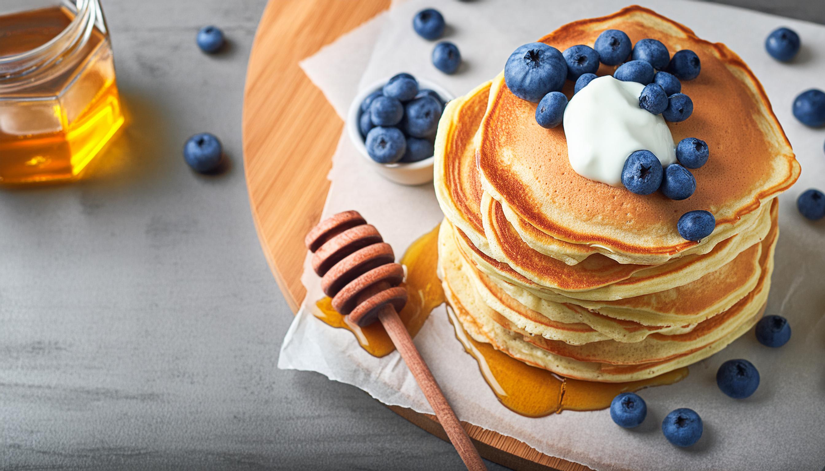 Stapel pannenkoeken met bosbessen, zure room en honing met een houten honingdipper.
