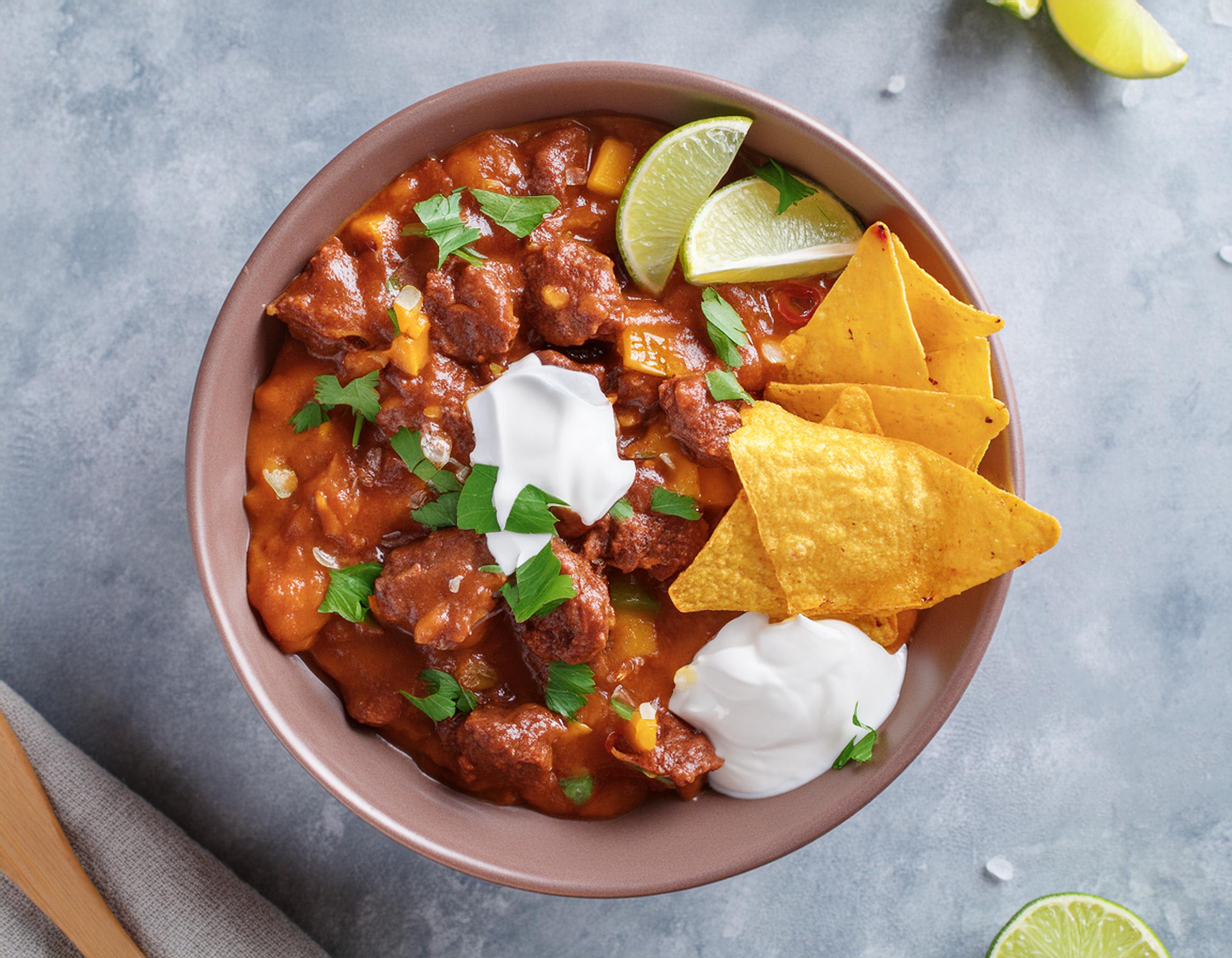Kom chili con carne met tortillachips, een dot zure room en partjes limoen.
