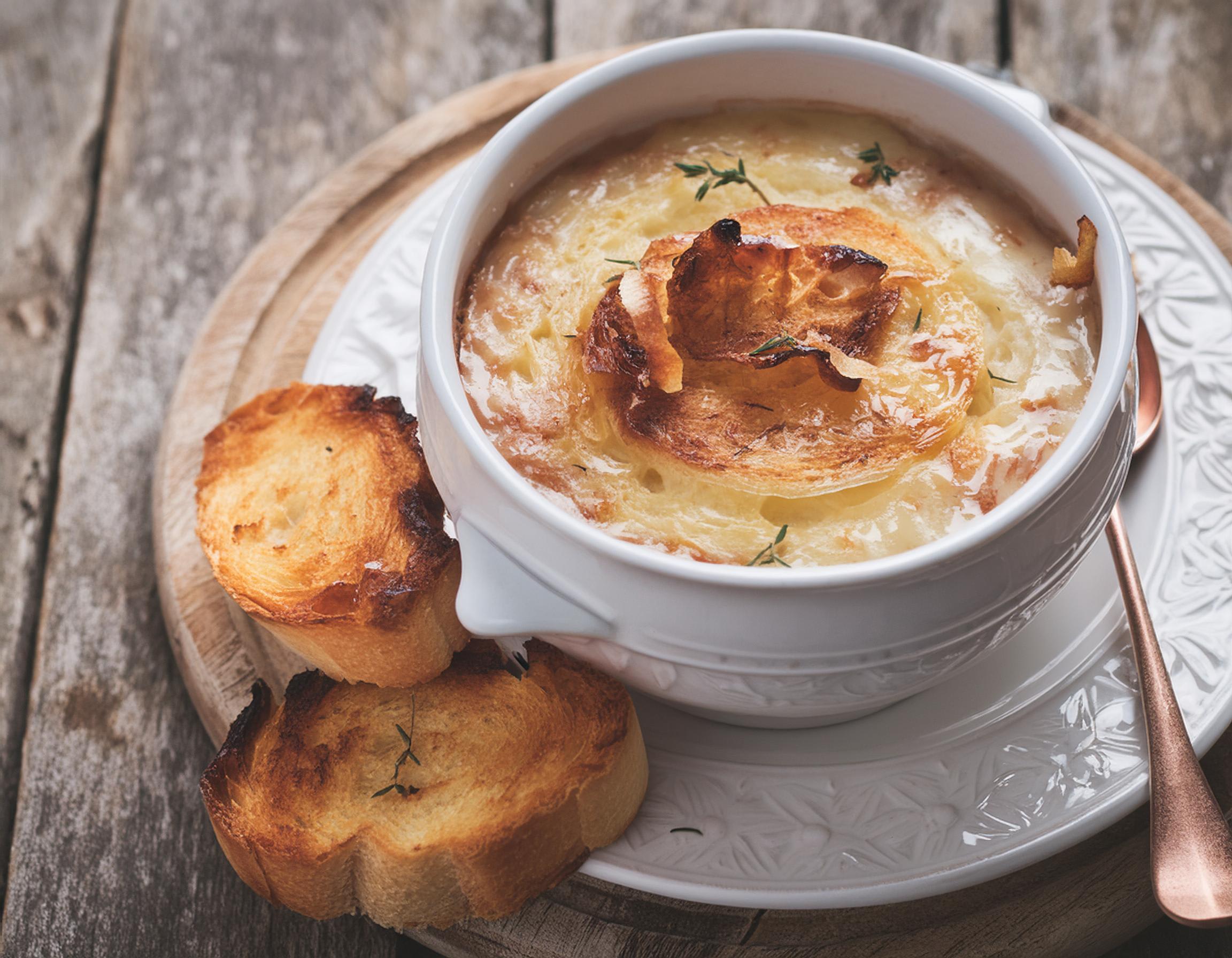 Kom uiensoep met een gesmolten kaaskruid en twee krokante kaascrostini's ernaast.