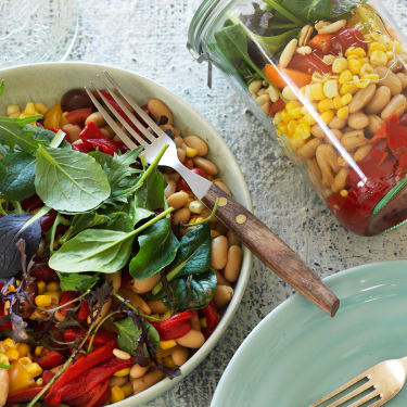 A colourful grain bowl on a table next to a jar.