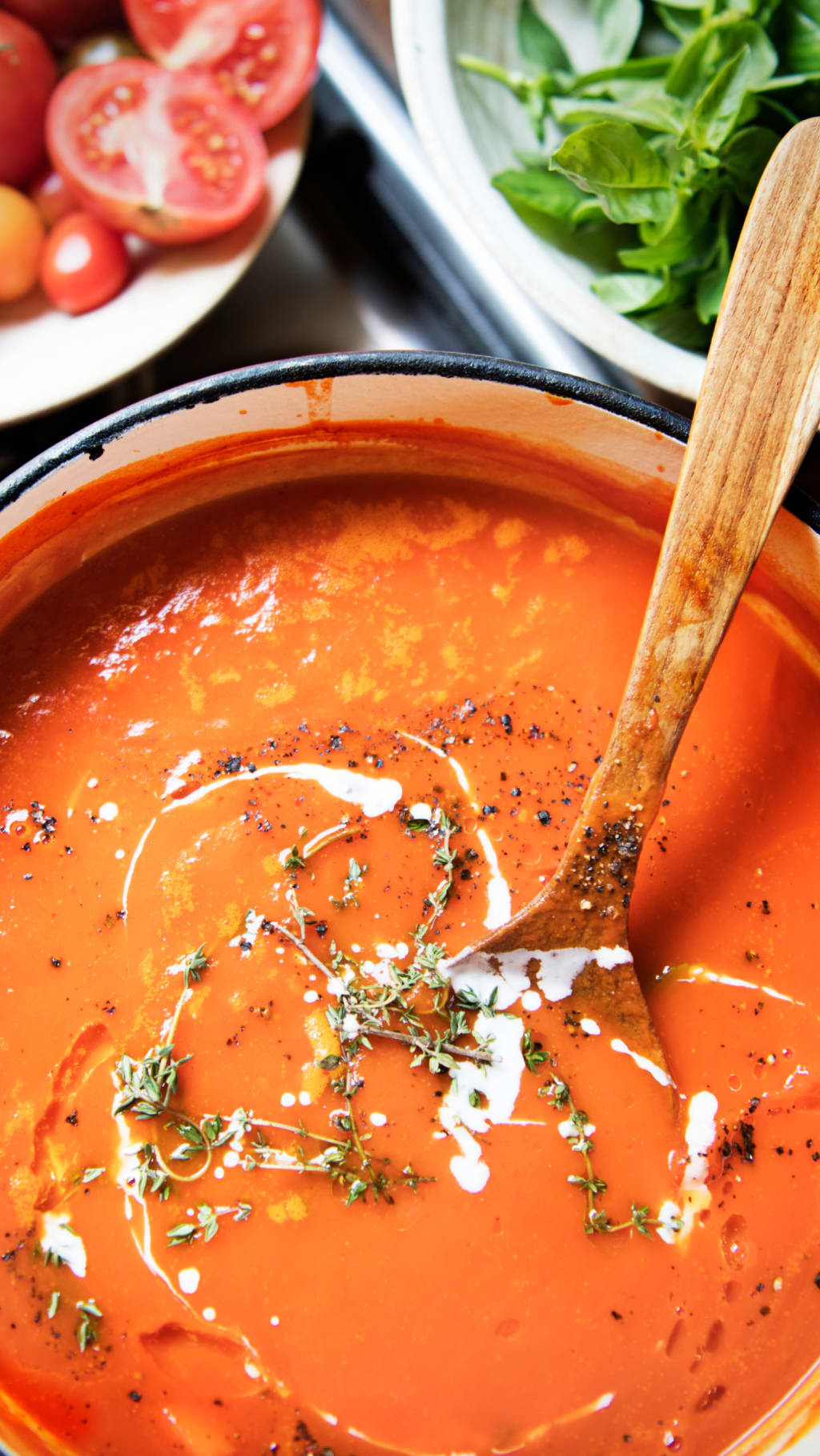 A large pot full of tomato sauce, next to a bowl of fresh tomatoes and basil.