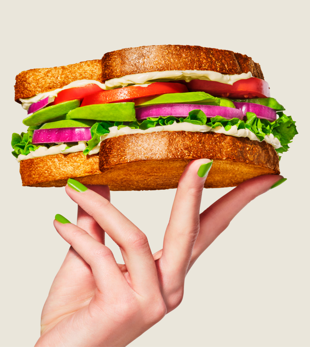 Une main tenant un sandwich avec de l'avocat, tomate, oignon et laitue.