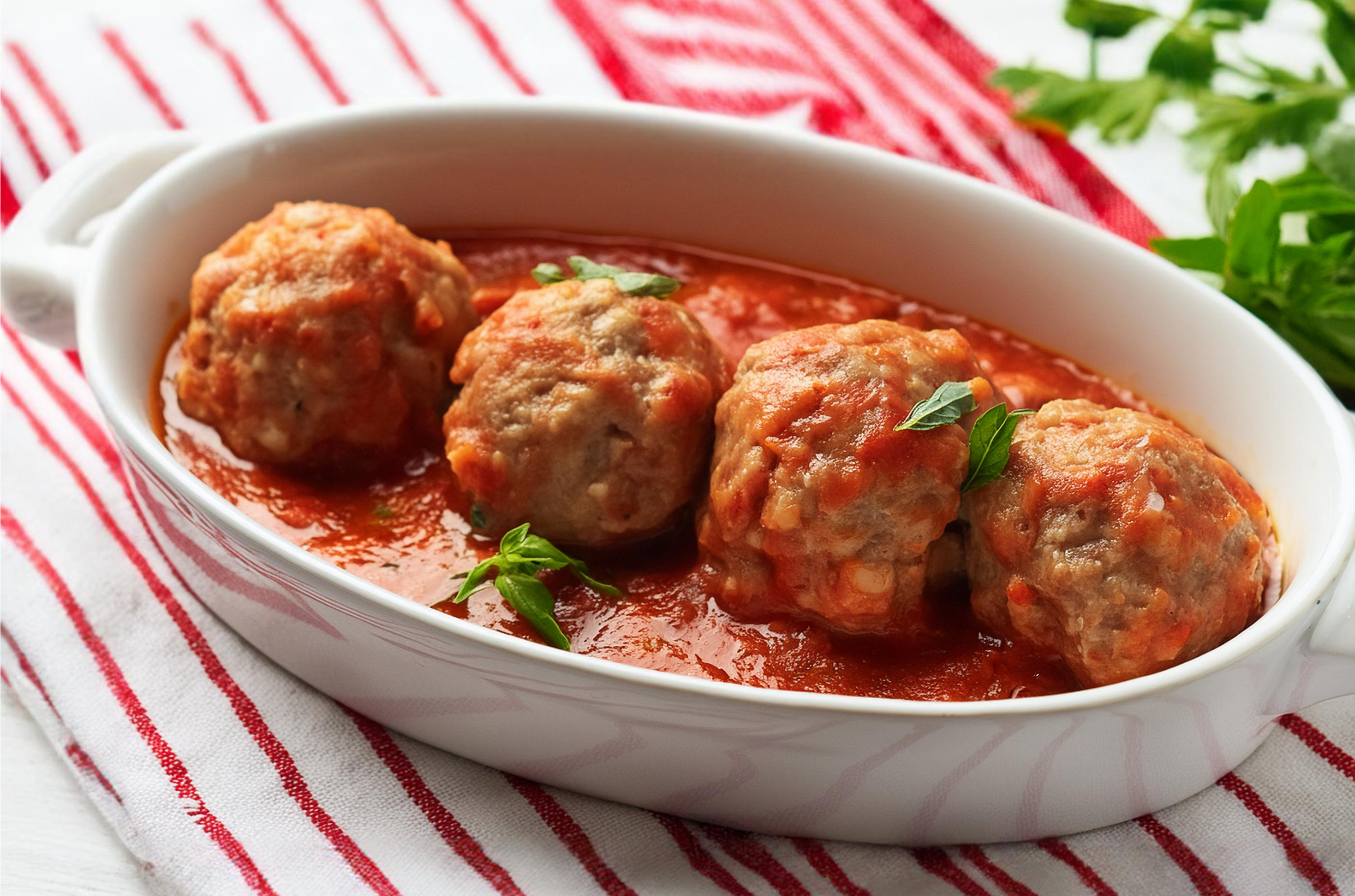 Klopsiki rybne w aromatycznym sosie pomidorowym podane w białym ceramicznym naczyniu.
