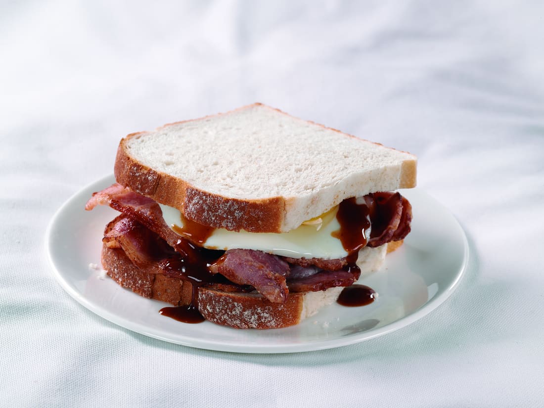 Bacon and egg sandwich with brown sauce on a white plate.