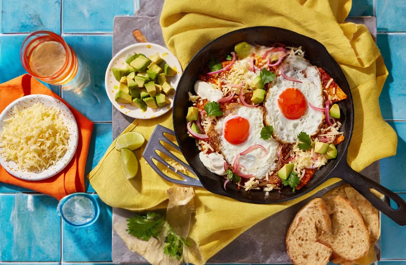 Two fried eggs over tortilla chips with red and green salsas in a skillet.