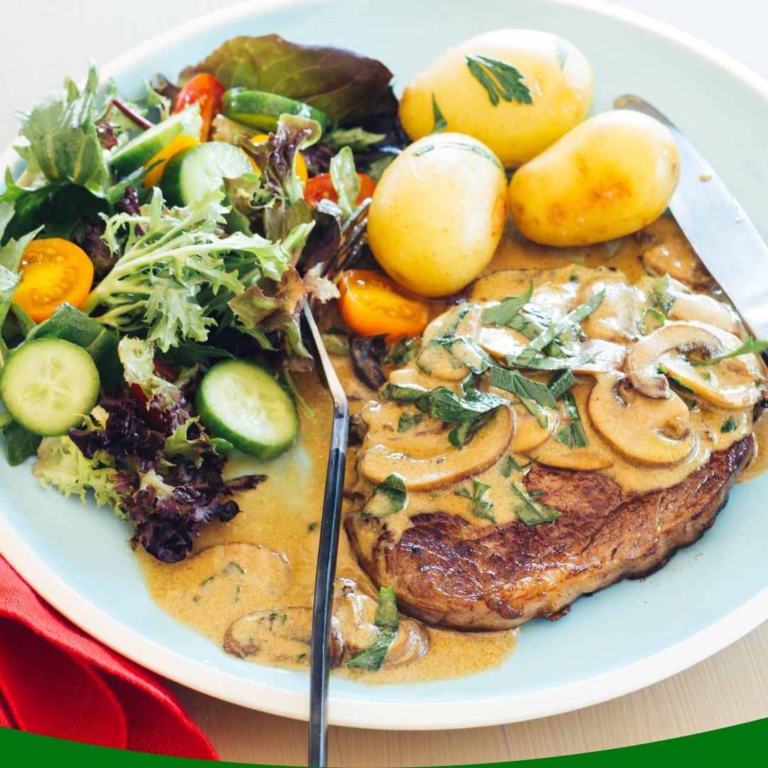 A dinner plate featuring steak, mushroom sauce, potatoes, and a salad.