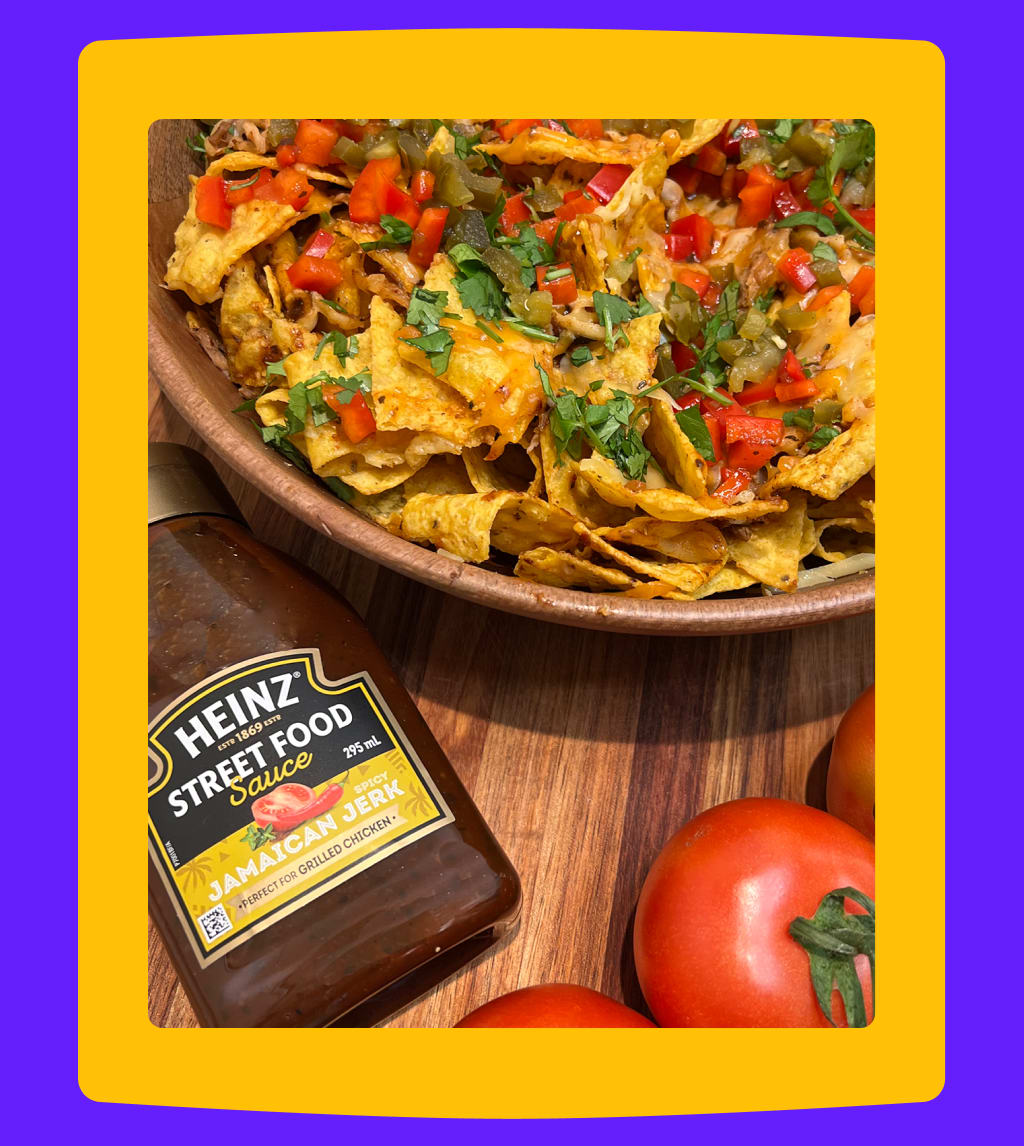 Bowl of nachos topped with Heinz Jamaican Jerk sauce and tomatoes.