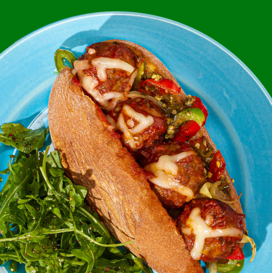 Meatball sandwich with cheese, peppers, and pesto on a blue plate.