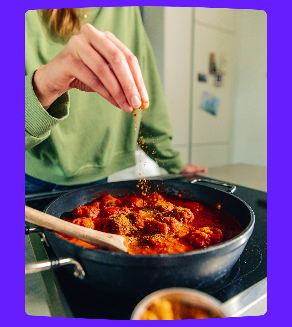 Person seasoning food in a pot with a wooden spoon.
