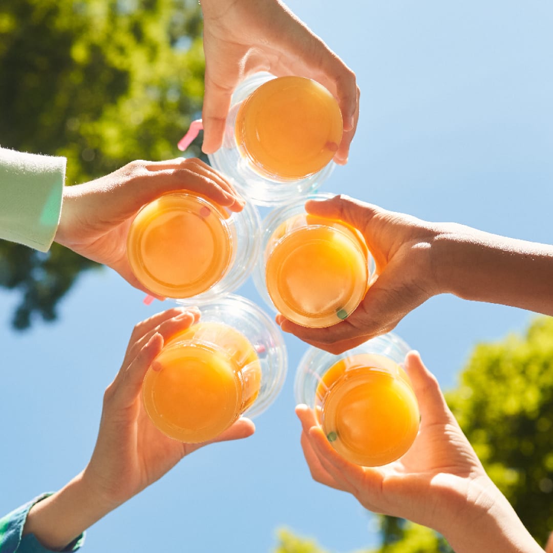 Five hands holding glasses of juice, joined together in a cheers.