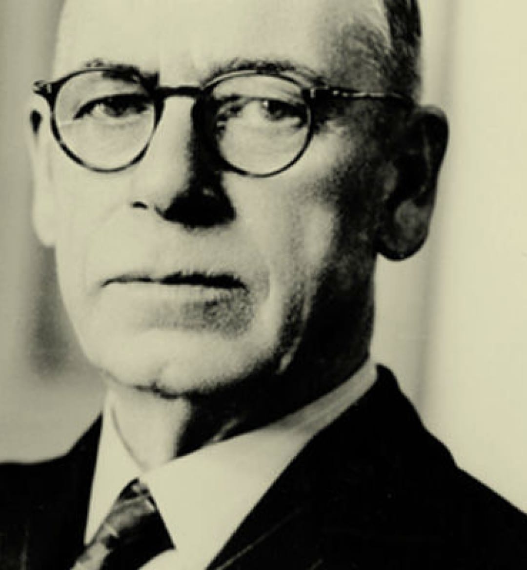 A black and white image of a man wearing glasses and a suit.