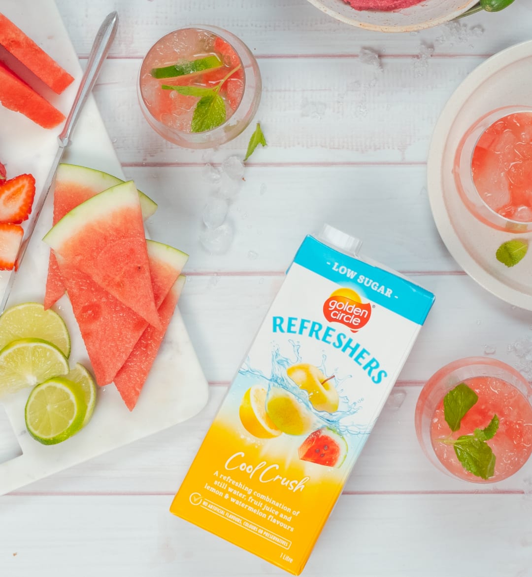 A top down shot of watermelon beverages next to sliced limes and watermelon and a box of Golden Circle Refreshers.