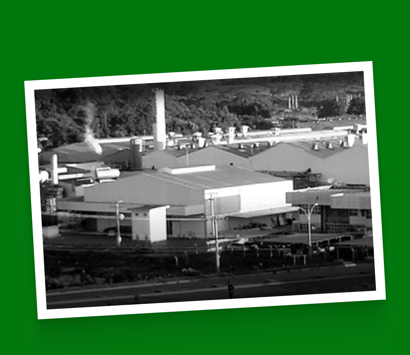 Imagem em tons de cinza de uma fábrica com fumaça saindo da chaminé.