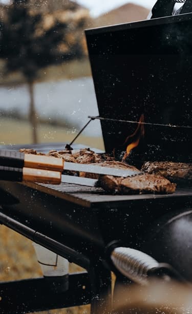 Eine Hand wendet Steaks auf einem offenen Grill.