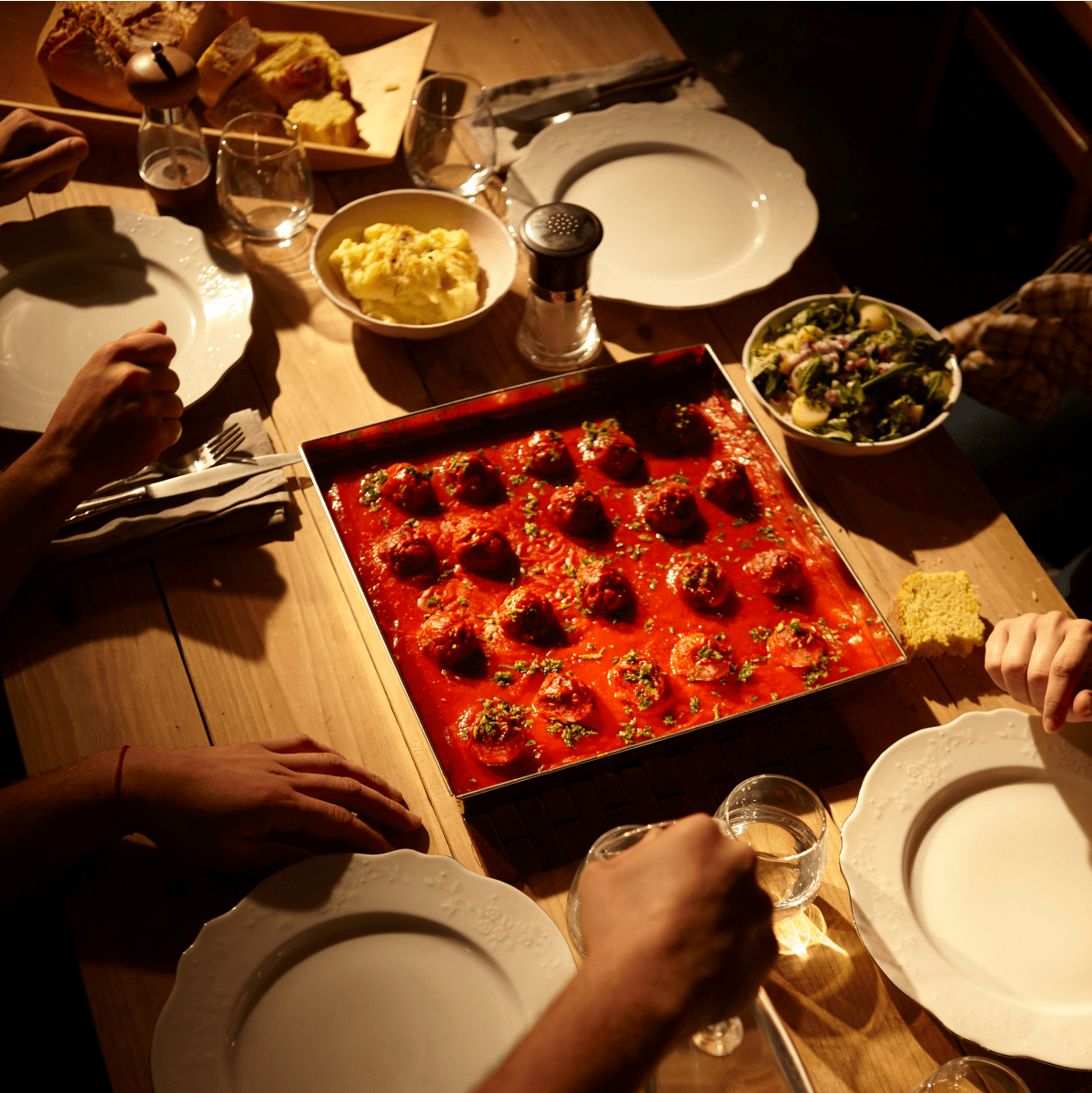 Imagen de una mesa de cena con albóndigas en salsa de tomate, platos y ensalada.