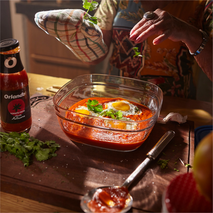Imagen de preparación de comida con huevos en salsa de tomate y una botella de salsa de tomate Orlando.