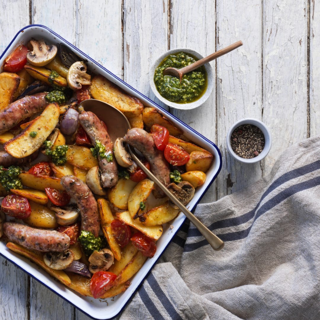 Bratwurst with potatoes, mushrooms, and tomatoes in a baking dish.