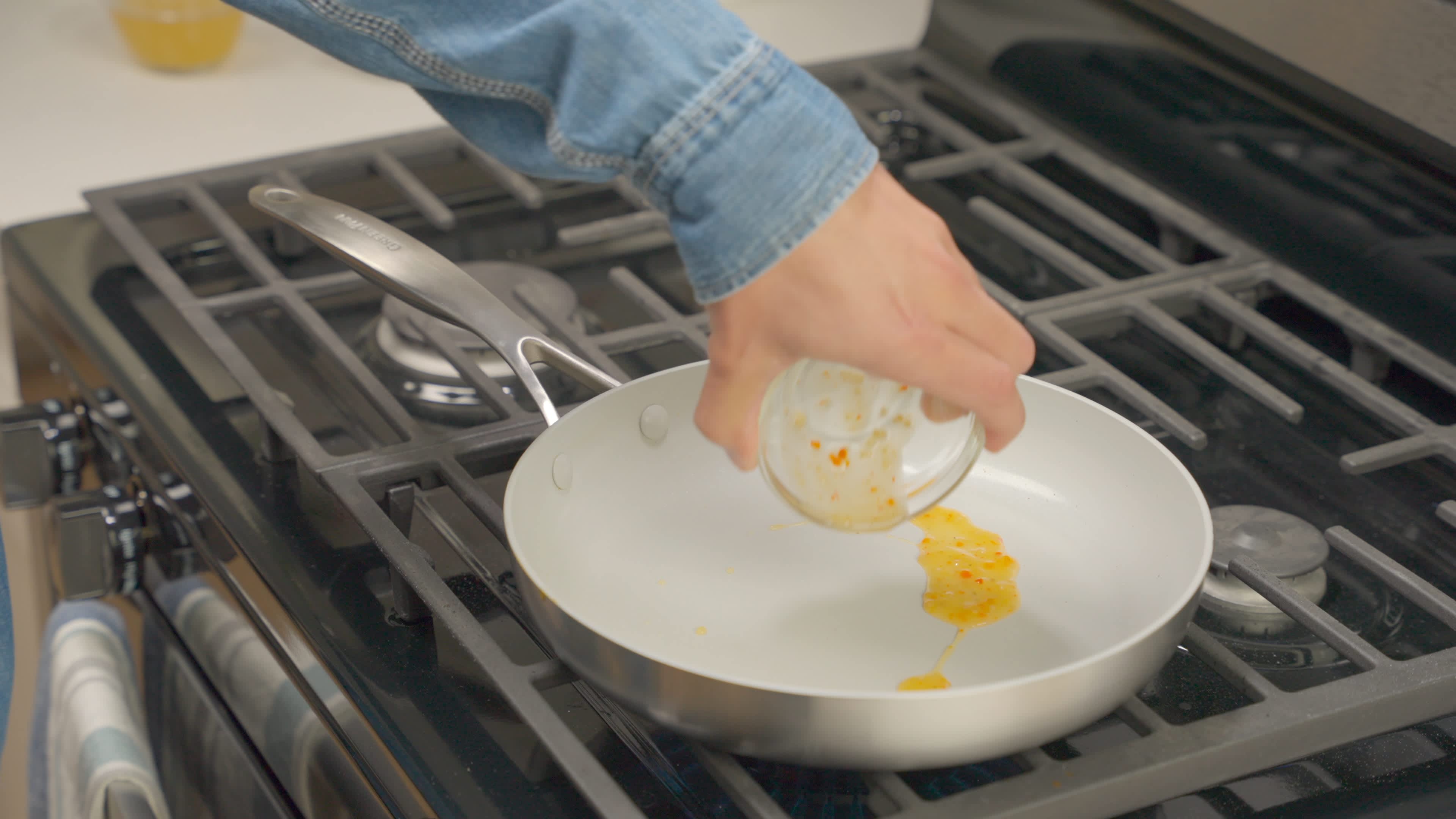 A large frying pan on a stove on medium-high heat showing a small bowl of dressing being poured into it.