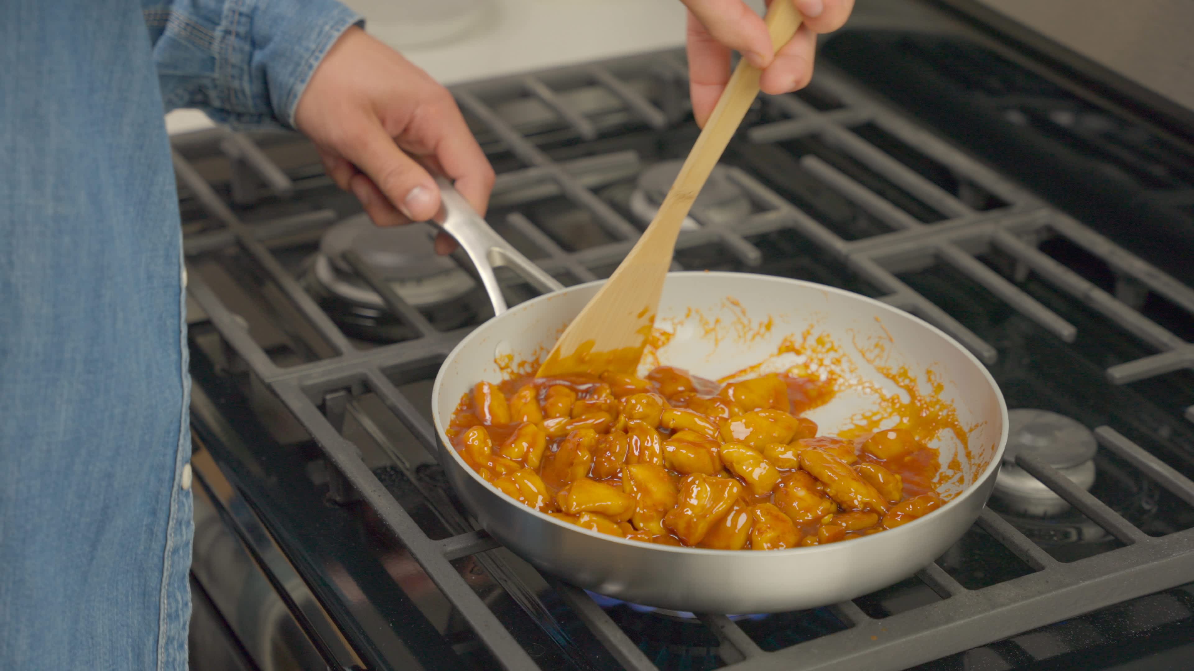 Slices of chicken cooking and being stirred in a frying pan over medium-high heat.