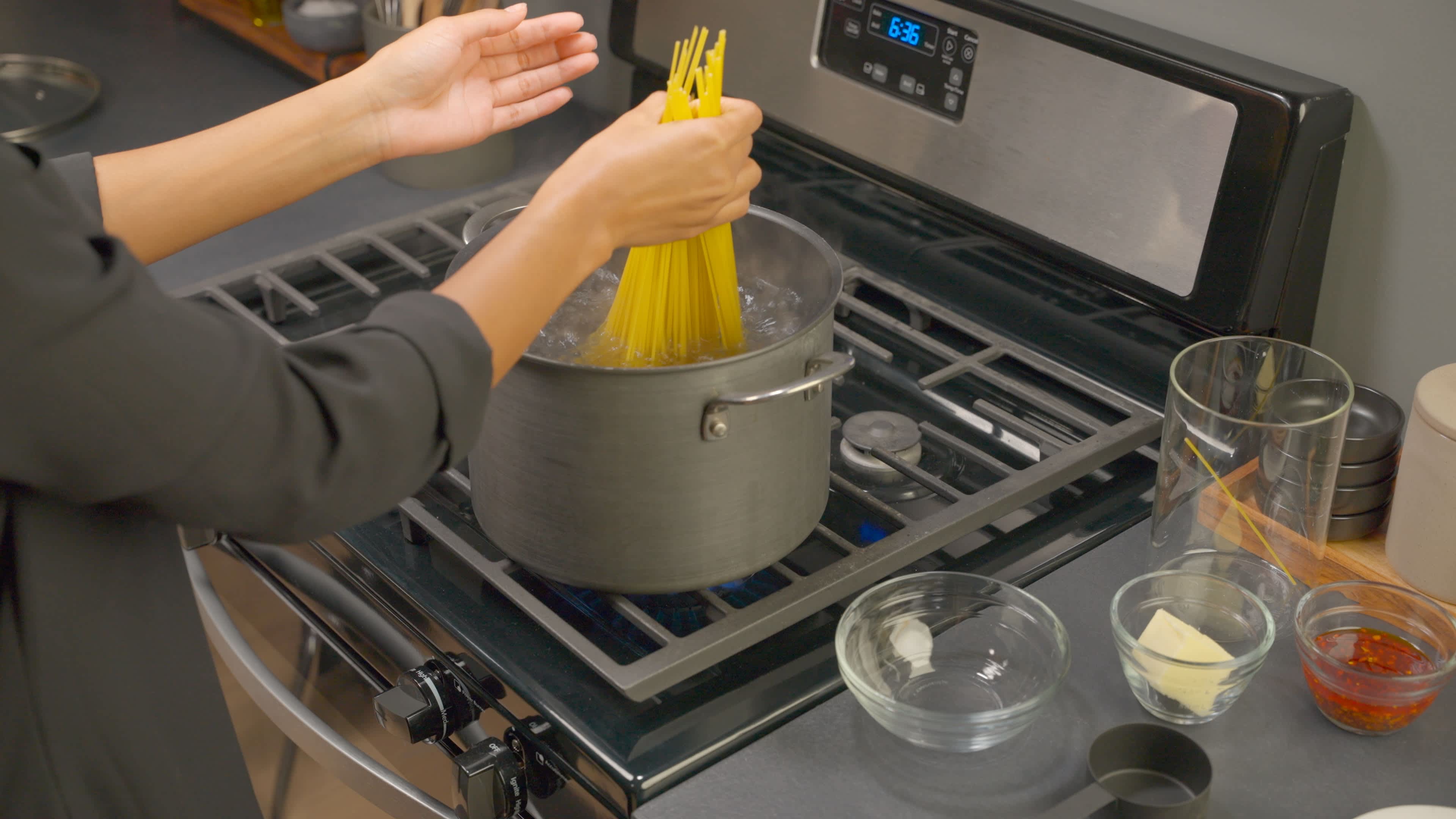 Spaghetti is added to a large pot of boiling water on the stove.