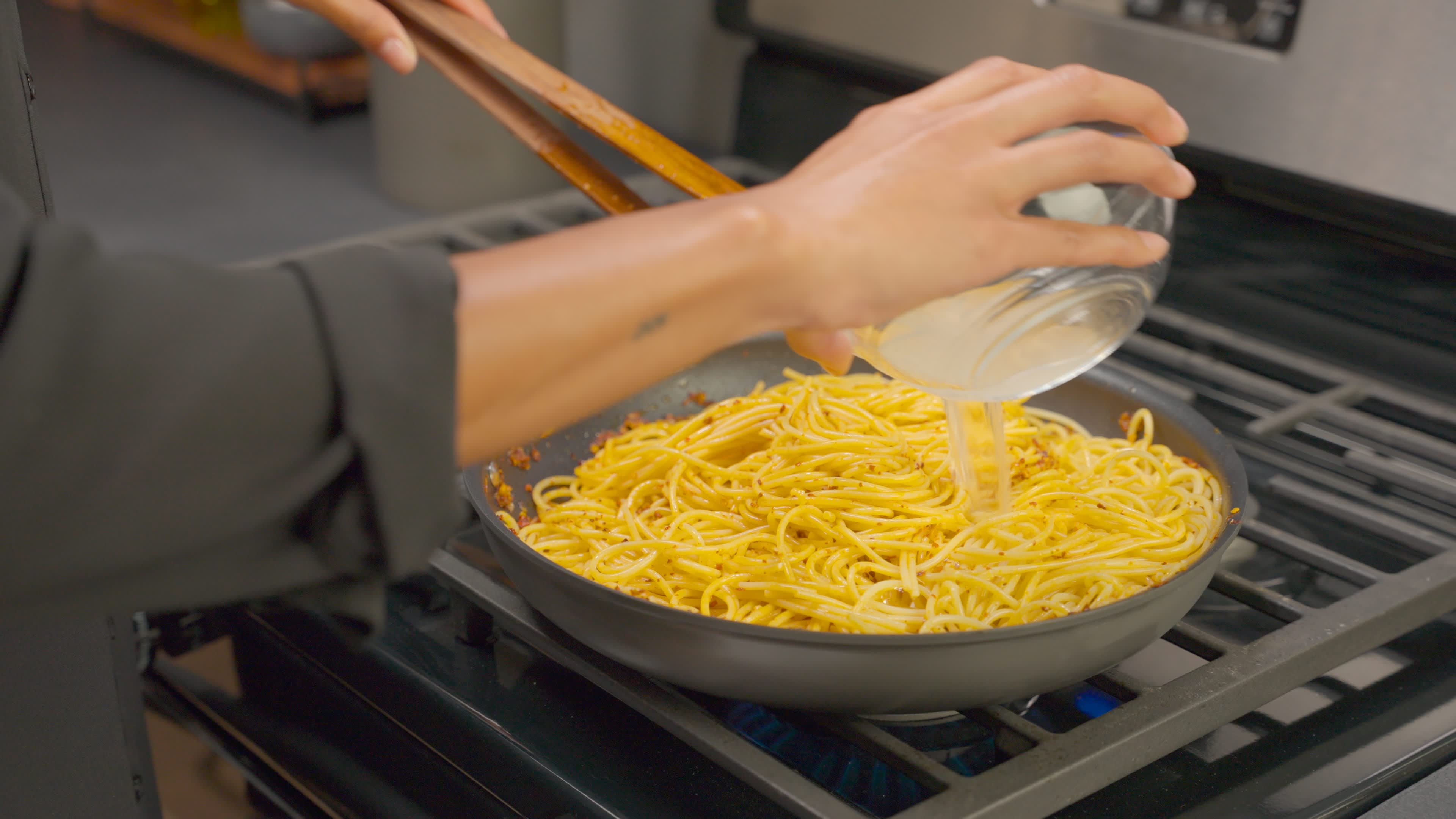 In the skillet, pasta is added to the Chili Pepper Crunch Sauce. Reserved cooking water is poured in.