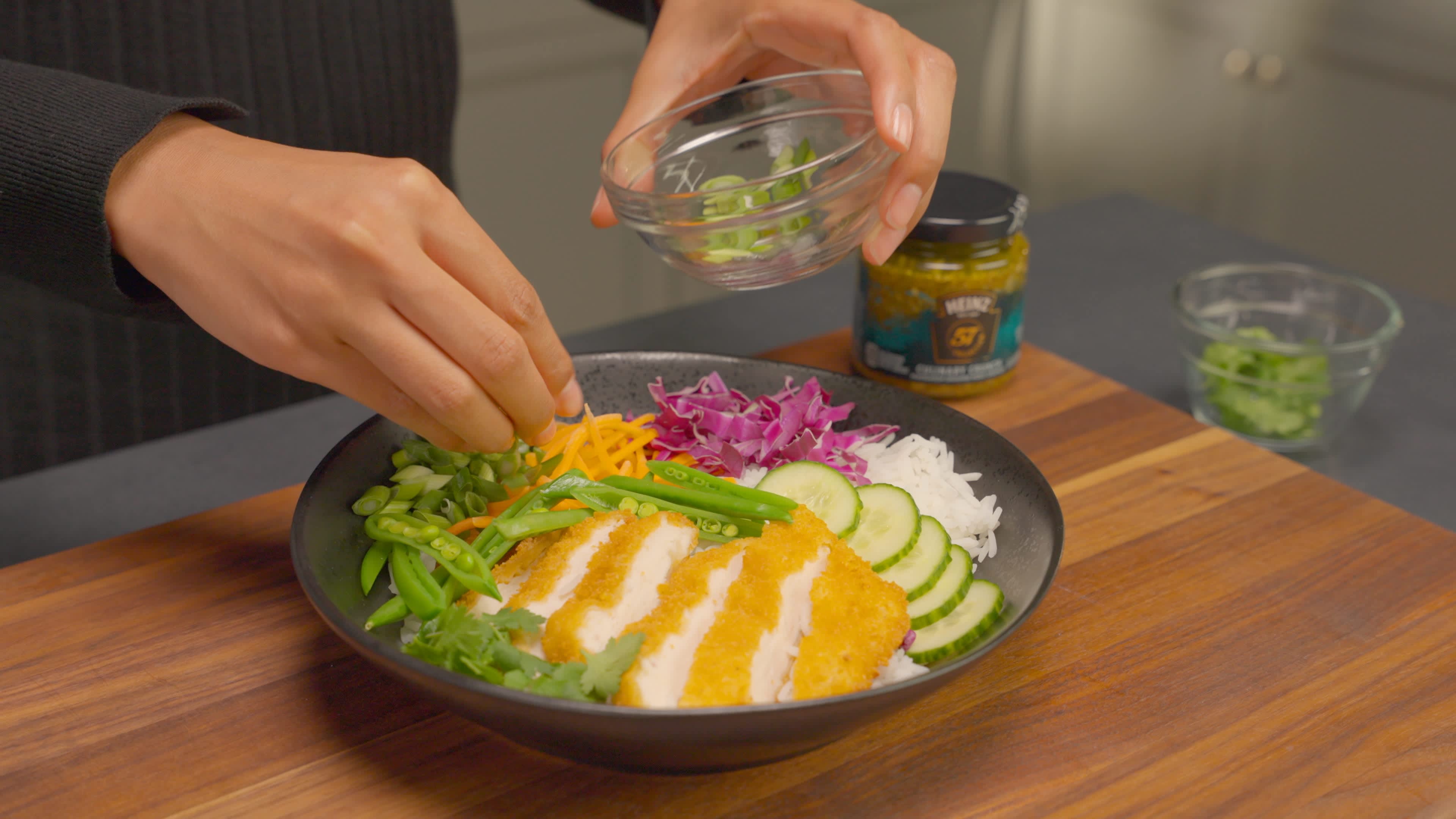 Vegetables and cilantro are spooned over the sliced chicken on the bed of cooked rice.