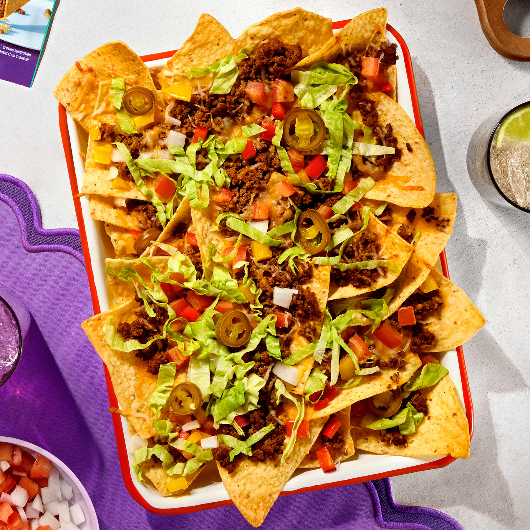 Loaded nachos with seasoned beef, melted cheese, lettuce, tomatoes, onions, and jalapeños in a white serving dish.