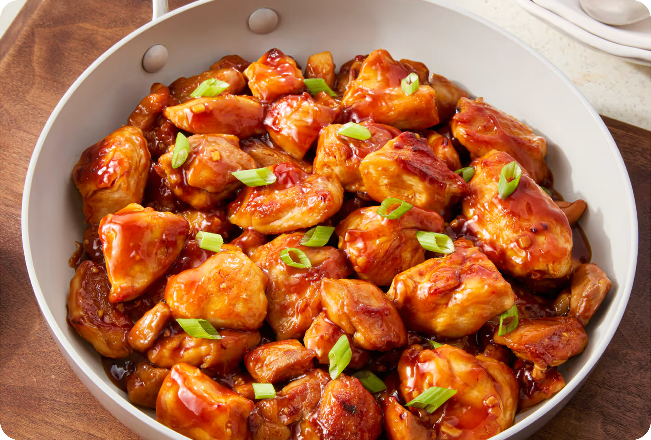 A skillet filled with glazed honey garlic chicken topped with green onions.
